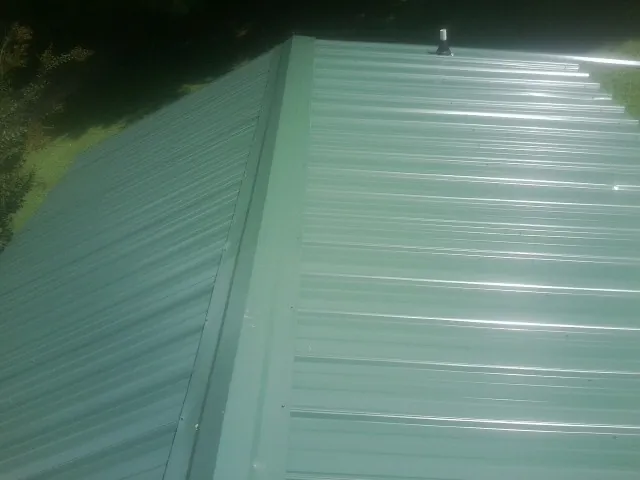 New green metal panels meeting at the ridge of a roof — Flat Roof Repair work by our crew in Hagerstown